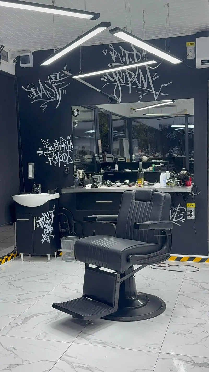 Postul de lucru din 13 Barbershop: scaun de frizerie din piele neagră, oglindă mare, pereți negri cu graffiti alb și lămpi LED.