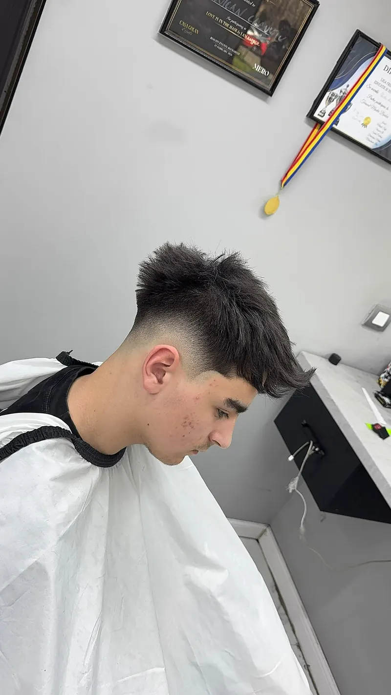 Client tânăr din profil, după tuns: fade scurt pe laterale, păr texturat lăsat mai lung sus.